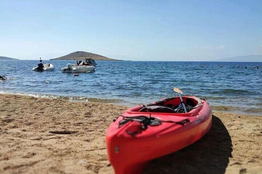 A red kayak on a sandy beach with boats in the water and a distant island. 2