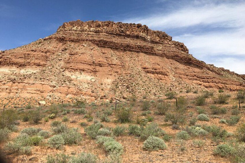 A large red rock formation with sparse vegetation in a desert landscape. 2