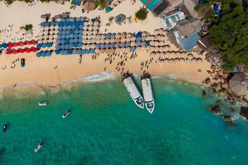 An aerial view of a beach with two boats anchored near the shore, surrounded by umbrellas and beach chairs. 3
