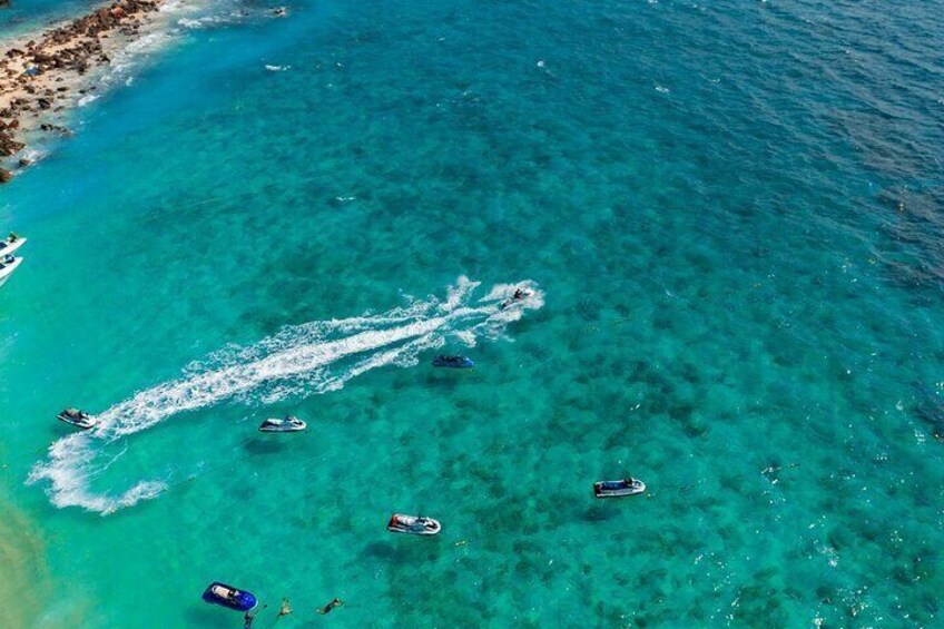 A clear turquoise sea with several boats and a jet ski. 2