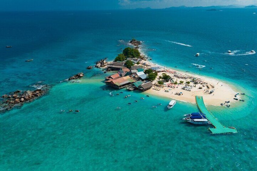 An aerial view of a tropical island with clear turquoise waters, a sandy beach, and a small settlement with buildings and boats. 4