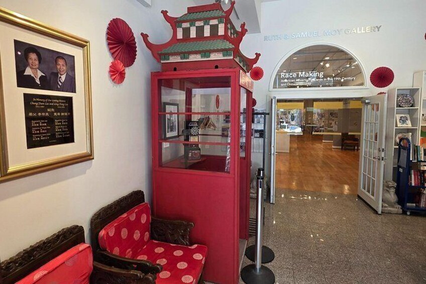 A gallery interior with a red display case, framed certificates, and a sign for 'Ruth & Samuel Moy Gallery'. 5