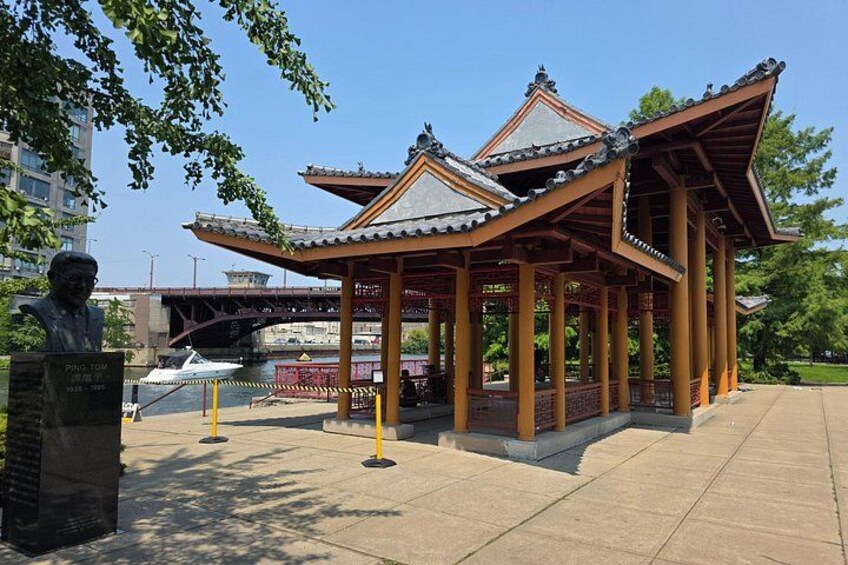 A traditional pavilion with a tiled roof, a statue, and a bridge in the background. 3