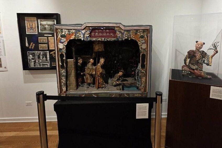 A framed historical painting with a decorative border, a small statue, and informational plaques. 2