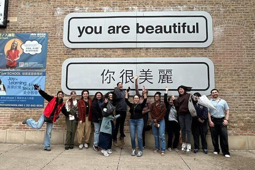 A group of people posing in front of a sign with the text 'you are beautiful' and another sign with Chinese characters. 1