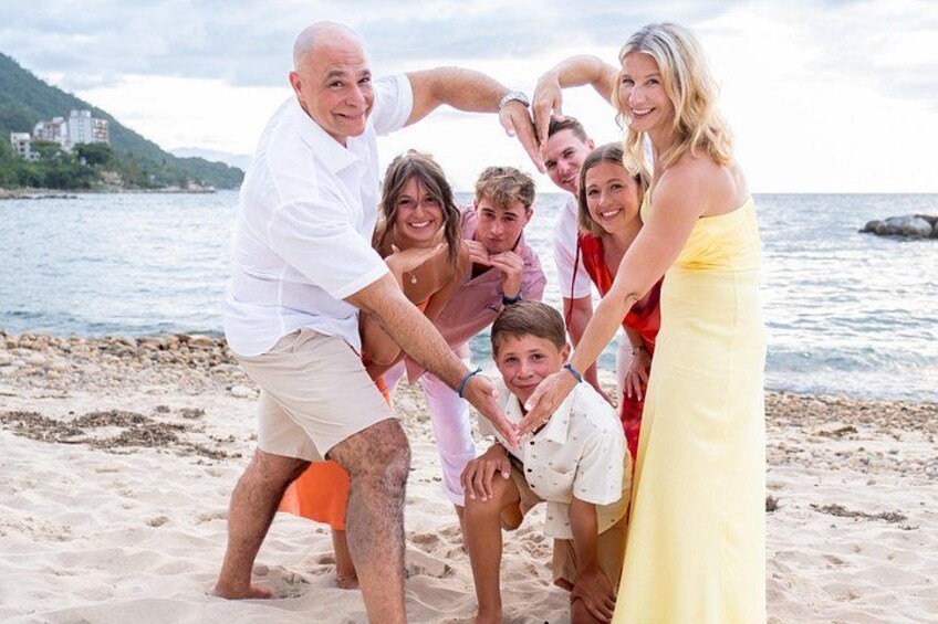 En familj på en strand med en stenig kust och en vattenyta i bakgrunden. 2