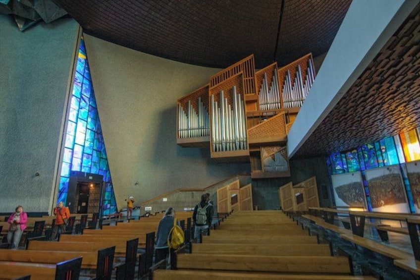 Ein Kircheninneres mit Holzbänken, einem Glasfenster und einer Orgel. 4