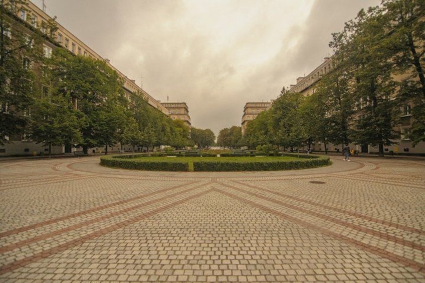 Ein gepflasterter Platz mit einem kreisförmigen Garten in der Mitte, umgeben von Bäumen und Gebäuden. 2