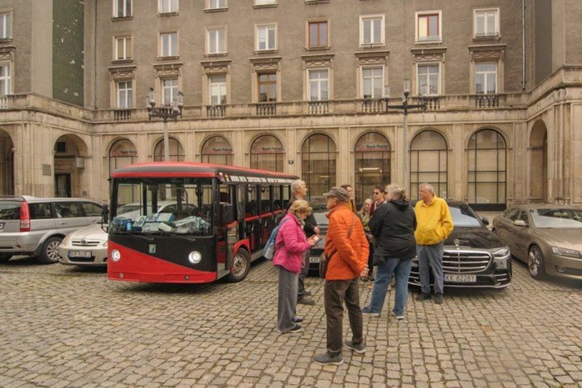 Ein roter Bus parkt vor einem Gebäude mit Rundbogenfenstern und einem Kopfsteinpflasterplatz. 1