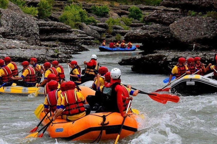 A group of people in inflatable rafts navigating a river with rapids. 1