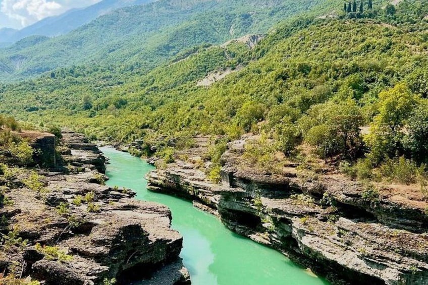 A river flowing through a rocky gorge with green water, surrounded by dense green forest and hills. 5