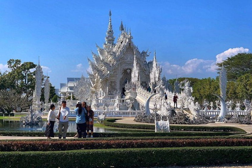A white ornate temple with a large central spire, surrounded by manicured gardens and visitors. 4