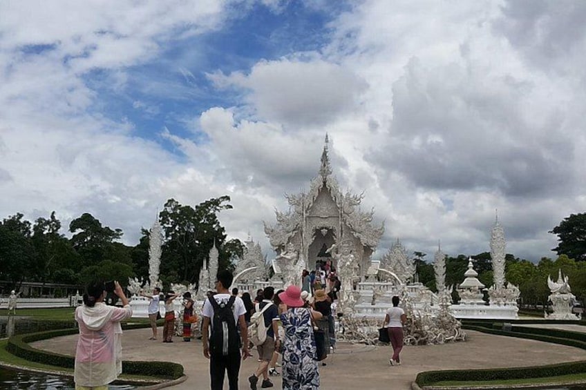A white temple complex with intricate architecture, surrounded by a well-maintained garden and a pond. 1