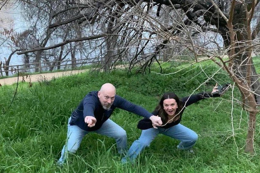 Two people crouching on grass near a tree and a body of water. 2