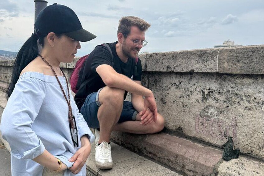 Two people sitting on a stone wall with a cityscape in the background. 1