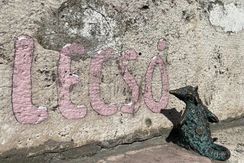 A stone wall with the word 'LEGO' painted in pink letters and a small green toy figure. 3