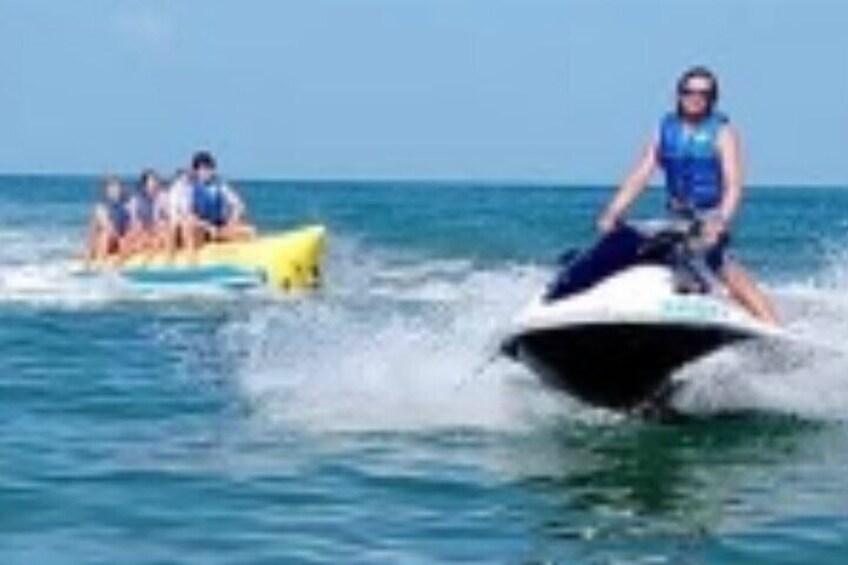 A person jet-skiing on the water with others in a yellow boat nearby. 2