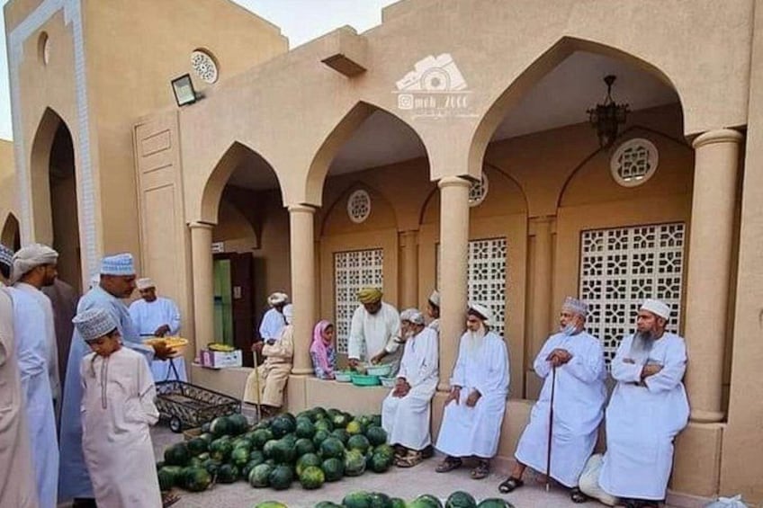 Un groupe de personnes, vêtues de costumes traditionnels, s’est rassemblé autour d’un bâtiment orné d’arches et de colonnes, et des pastèques étaient disposées sur le sol. 1