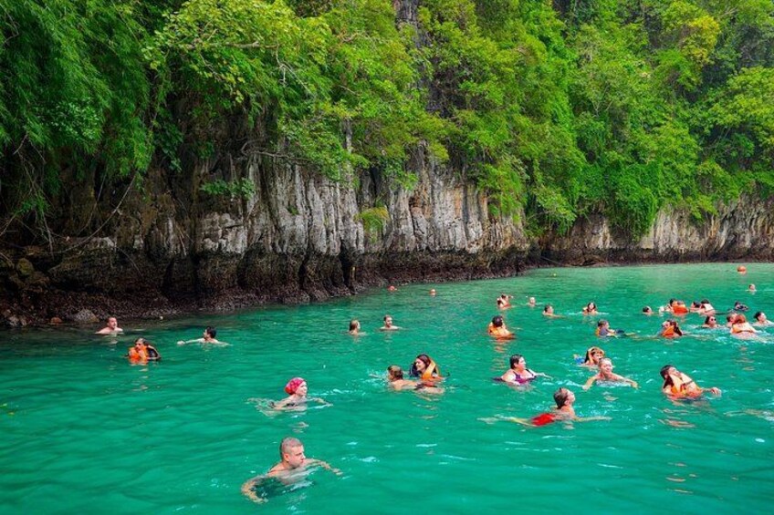 People swimming in a turquoise sea surrounded by lush greenery and rocky cliffs. 4