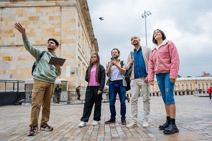 A group of people standing on a paved area with a historic building in the background. 1