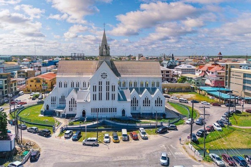 A large white church with a pointed steeple, surrounded by a parking lot and urban buildings. 2