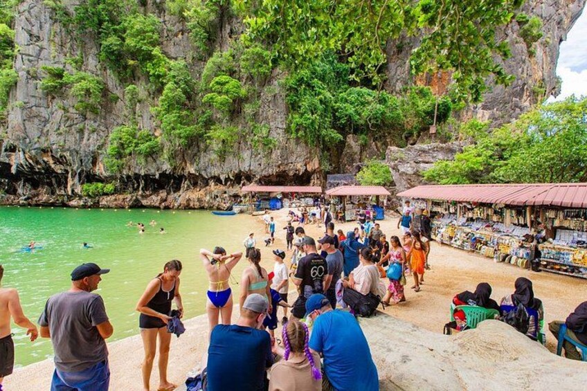 A crowded beach with people swimming and standing, surrounded by rocky cliffs and lush greenery. 3