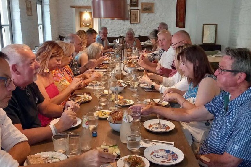 Un grupo de personas sentadas alrededor de una mesa larga, comiendo y bebiendo. 4