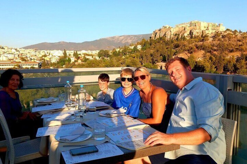Un grupo de personas cenando en una mesa con vistas panorámicas a un edificio histórico y montañas al fondo. 1