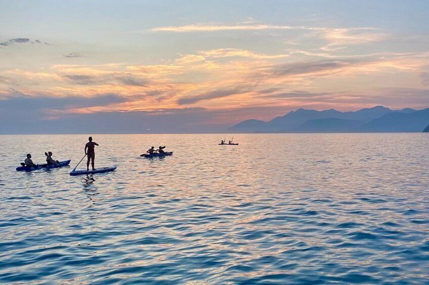 A calm lake with people paddling in small boats during sunset. 2