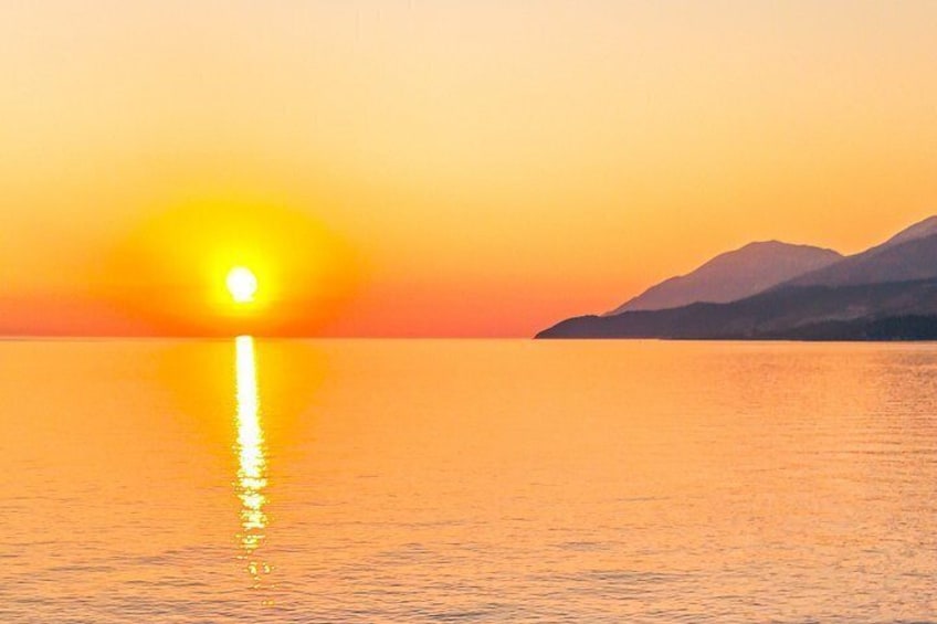 A sunset over a calm sea with mountains in the background. 5