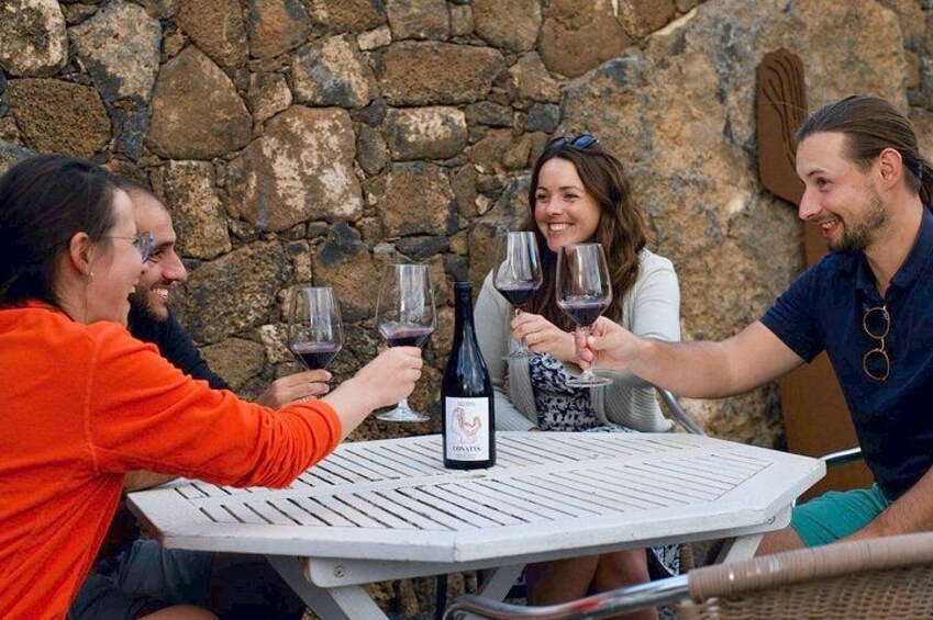 A group of people toasting with wine glasses around a table with a bottle of wine. 1