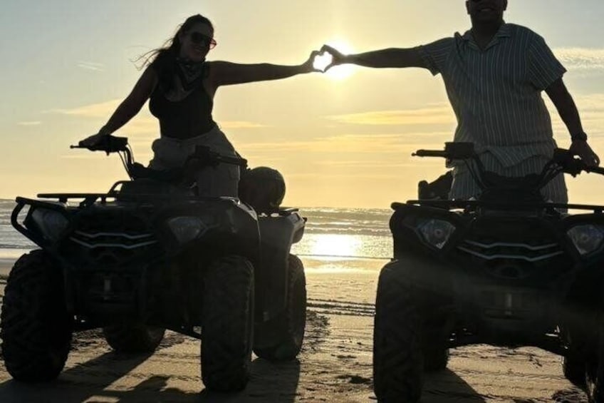 Due persone su quad ricreativi su una spiaggia, con il sole che tramonta sullo sfondo. 1