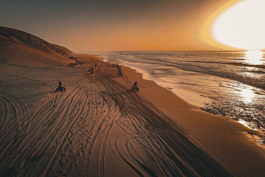 Paesaggio desertico con un tramonto, dune di sabbia e impronte che conducono all'acqua. 5