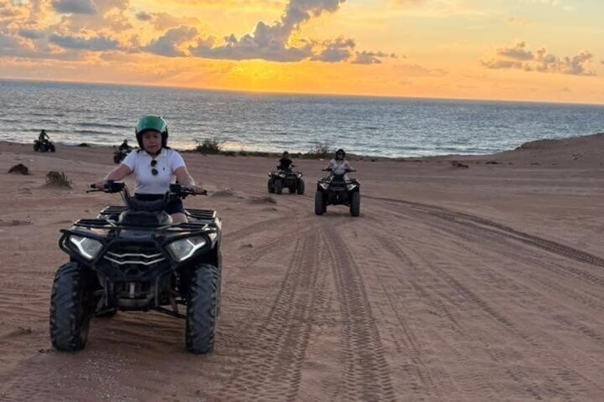 Una persona guida un ATV su un sentiero sabbioso, con l'oceano sullo sfondo. 4