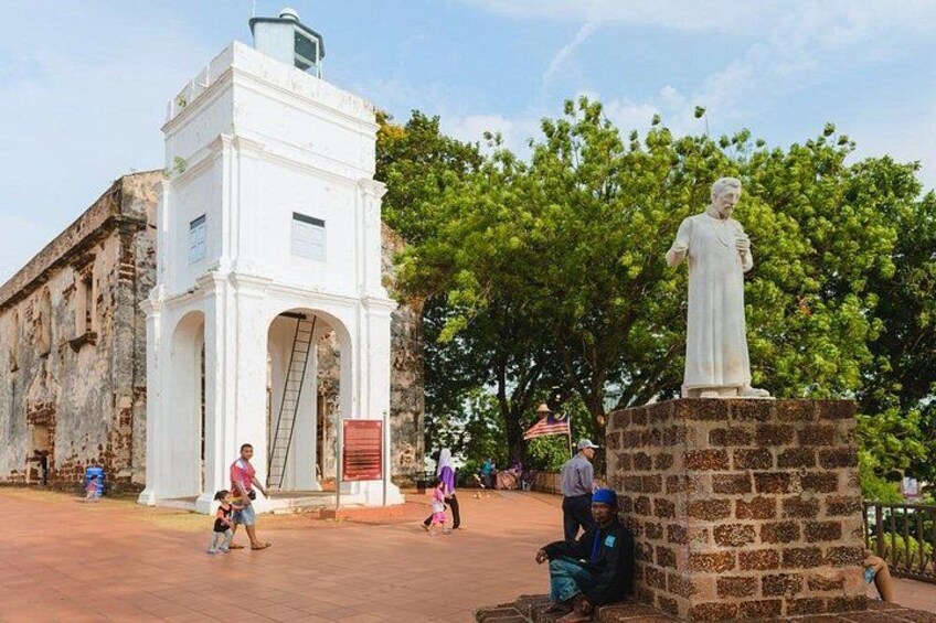 A historical building with a statue, a white tower, and a paved area with people. 5