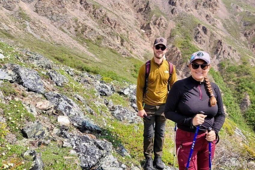 Two hikers on a rocky mountain trail with a grassy incline and rocky outcrops. 4