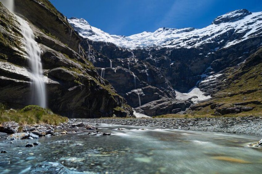 A mountain landscape with a waterfall, a river, and snow-capped peaks. 2