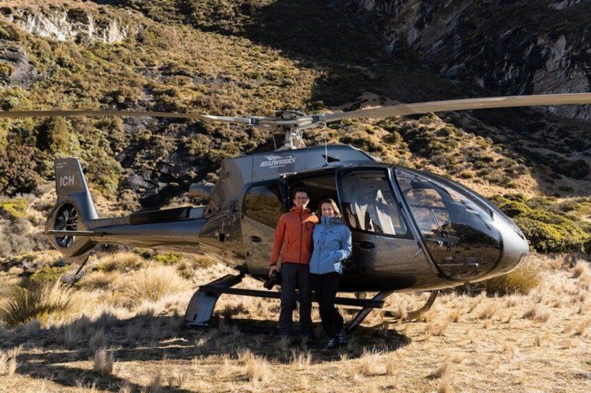 A helicopter with 'BILLYBOB'S' on its side parked on a grassy field with a rocky hillside in the background. 4