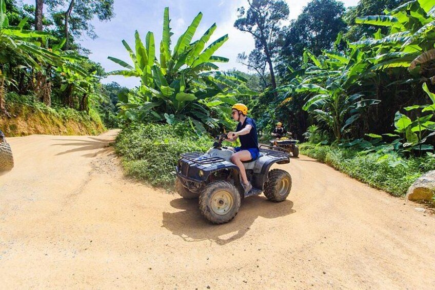 Een persoon op een quad op een onverharde weg, omringd door weelderige begroeiing. 5