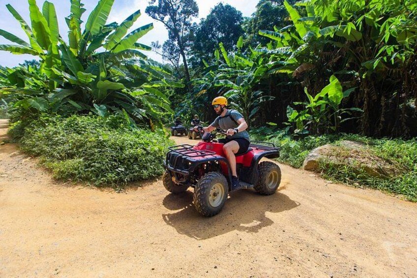Iemand rijdt op een quad op een zandpad, omringd door weelderige begroeiing. 4