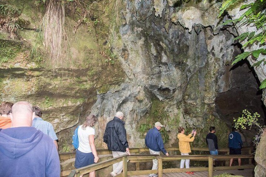 People standing on wooden stairs near a rocky cave entrance. 3