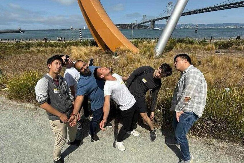 A group of people standing near a large sculpture and a bridge in the background. 3