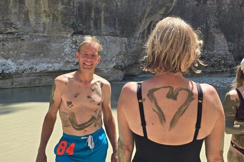 Two people with tattoos, one with a heart design on their back, standing near a rocky cliff. 5