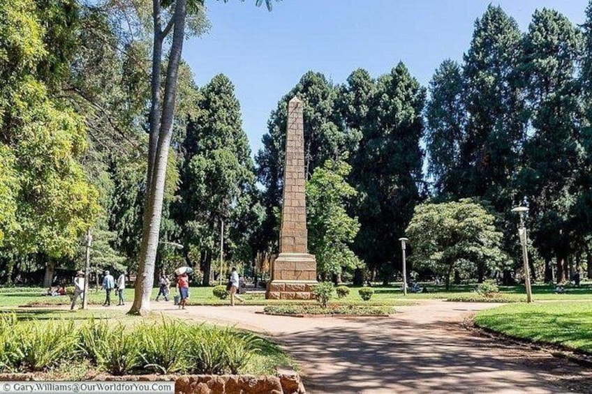 A park with a tall monument, trees, and a pathway. 3