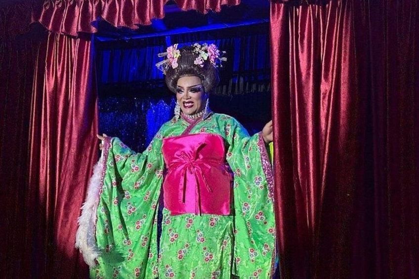 Una persona in costume tradizionale con un grande fiocco rosa, in piedi di fronte a una tenda rossa. 4