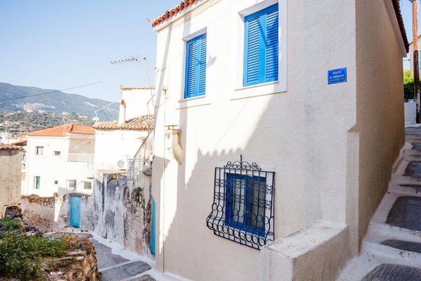 Una calle estrecha con edificios blancos, contraventanas azules y un letrero que indica un lugar. 4