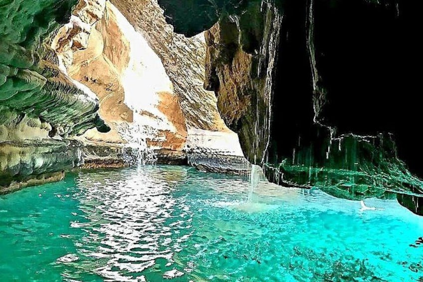 A cave with a waterfall, clear turquoise water, and rocky walls. 1