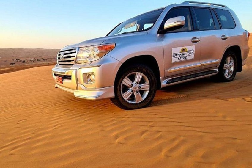 A silver SUV on a sandy terrain with a desert landscape in the background. 2