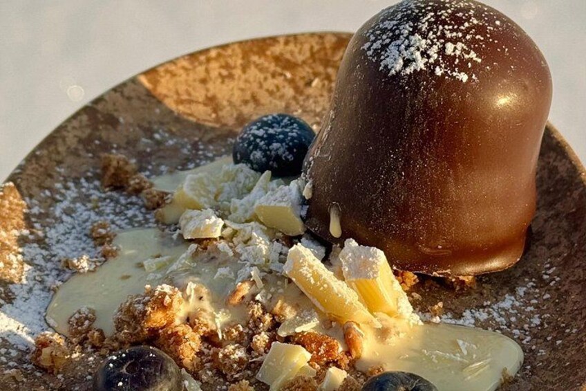 A dessert with a chocolate sphere, blueberries, and crumbled nuts on a plate. 5