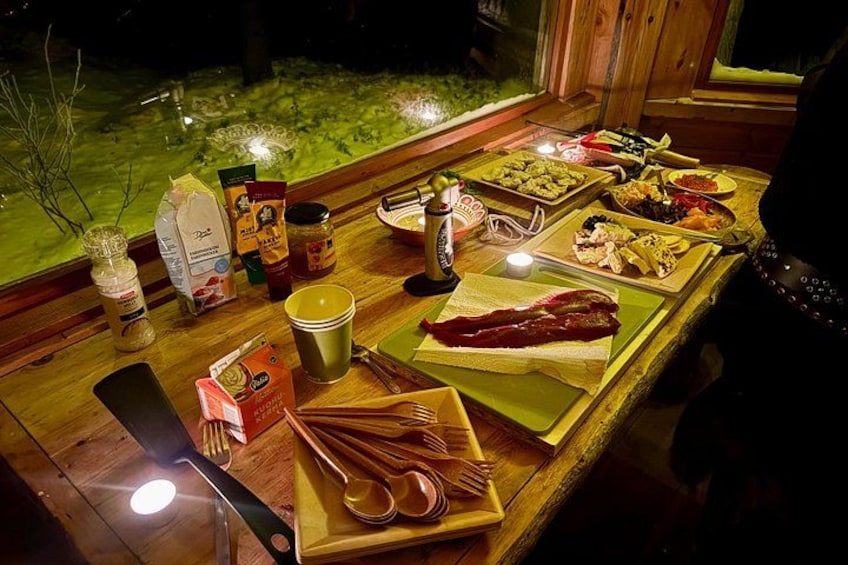 A wooden table with various food items and condiments, illuminated by candlelight. 4